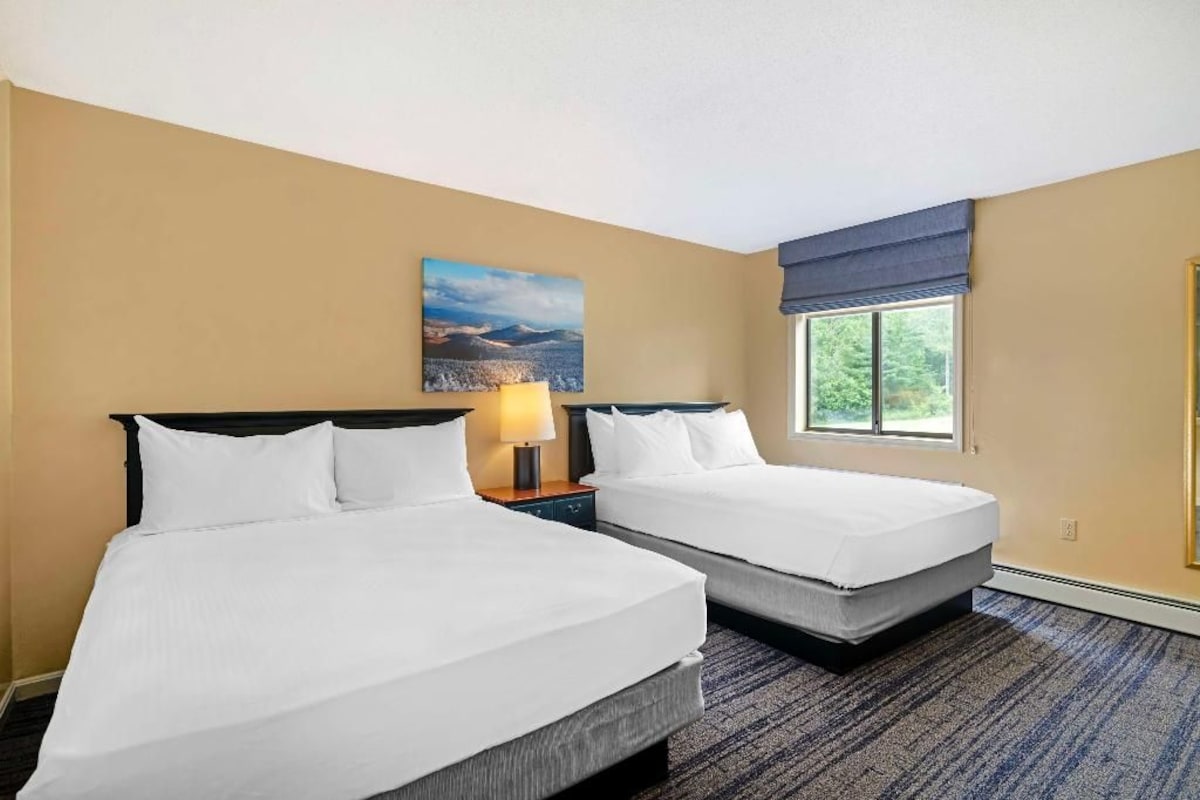 A hotel room with two beds, a window with a view, and a painting on the wall.