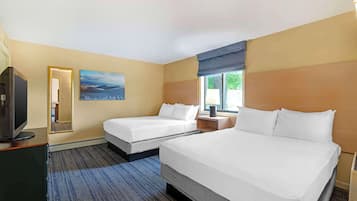 Habitación de hotel con dos camas, televisión, un cuadro y ventana con vista a árboles.