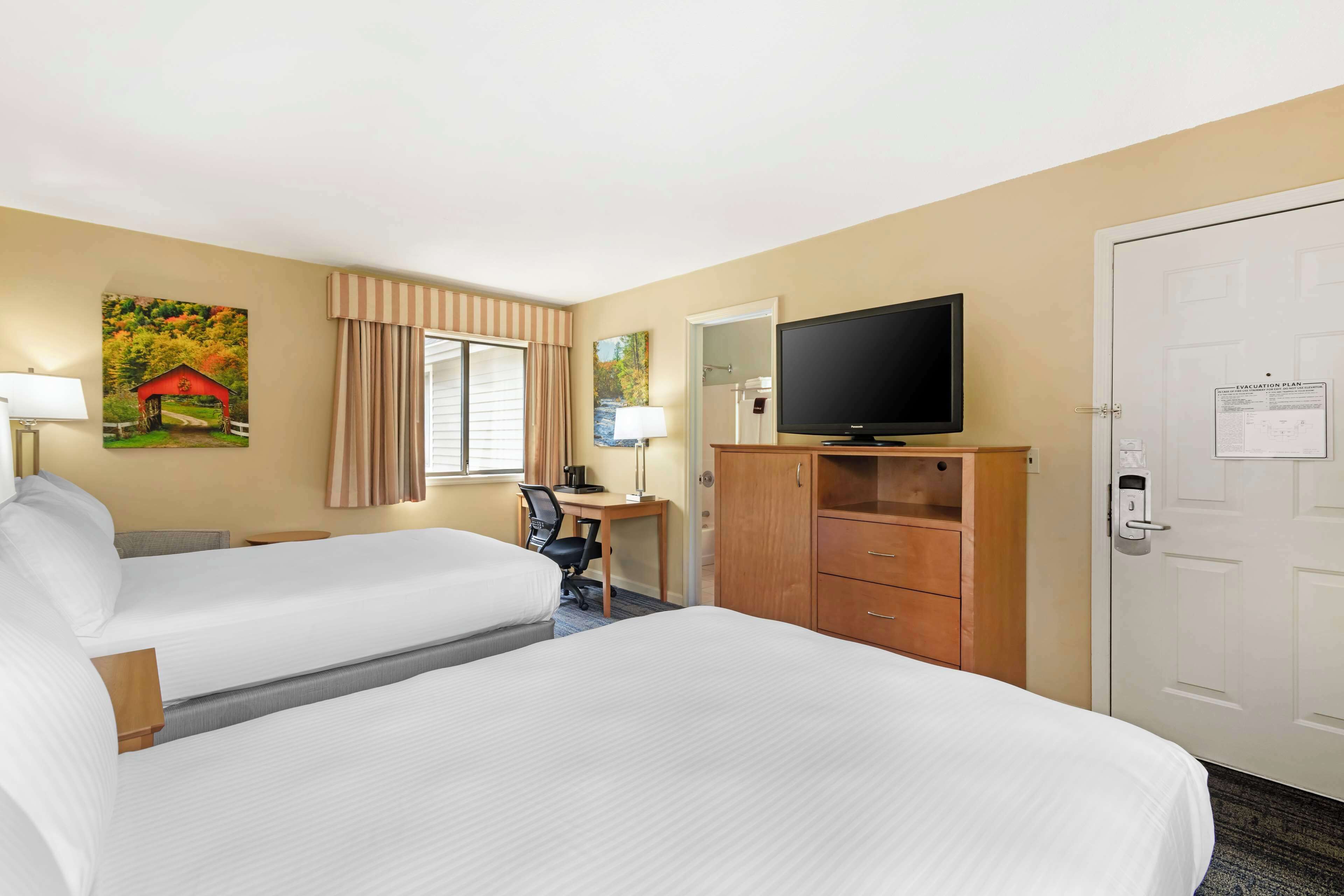 A hotel room with two beds, a desk with a chair, a television, and a wardrobe.