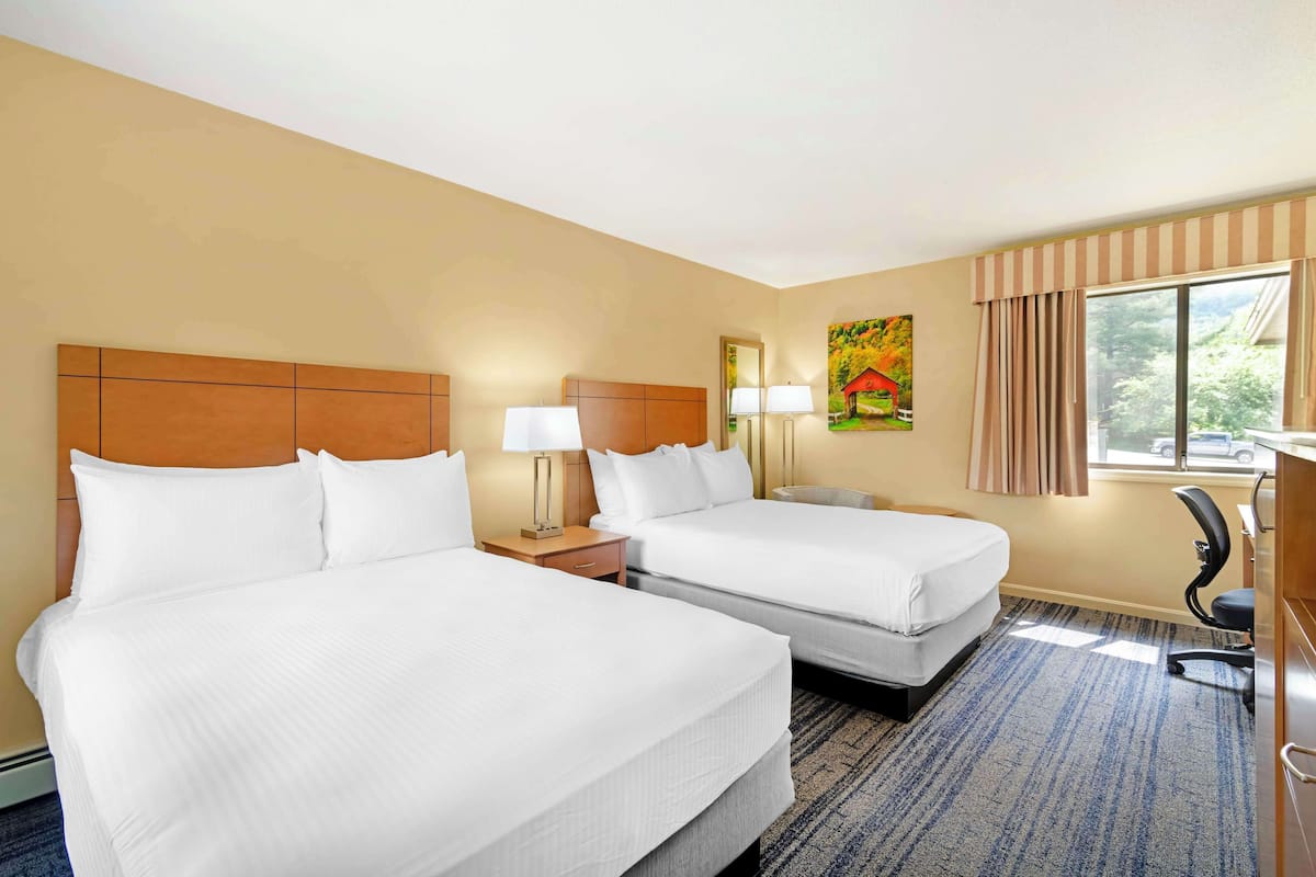 A hotel room with two beds, a desk, a chair, a window with curtains, and a painting on the wall.