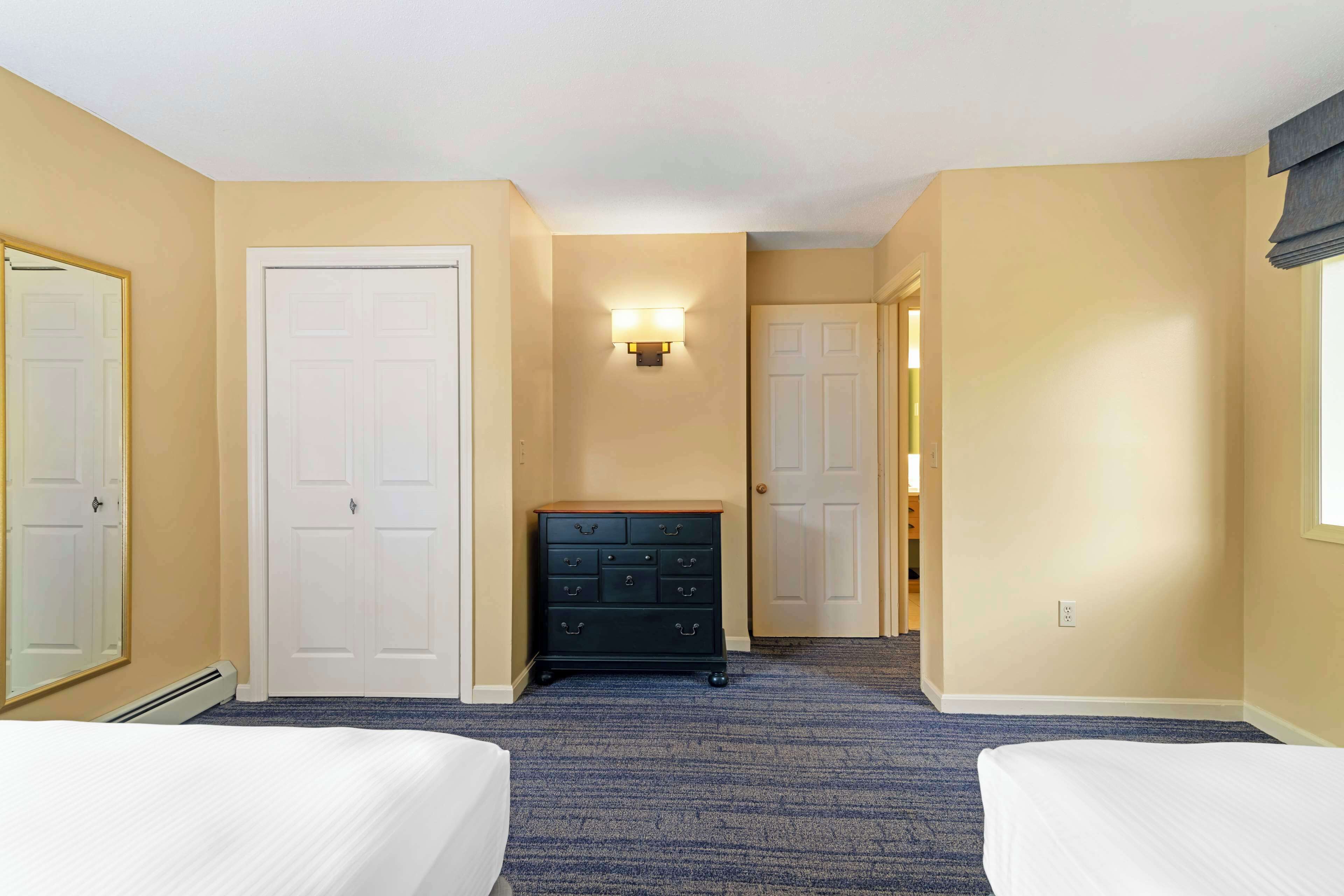 A hotel room with two beds, a dresser, and a hallway leading to another room.
