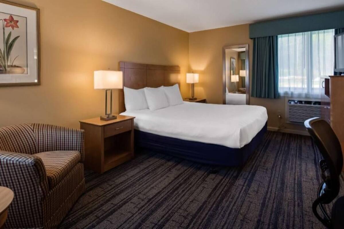 A hotel room with a large bed, two bedside tables with lamps, a chair, a desk, and a television.