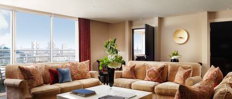 A spacious living room with a large window offering a city view, a white coffee table, and two beige sofas with patterned cushions.
