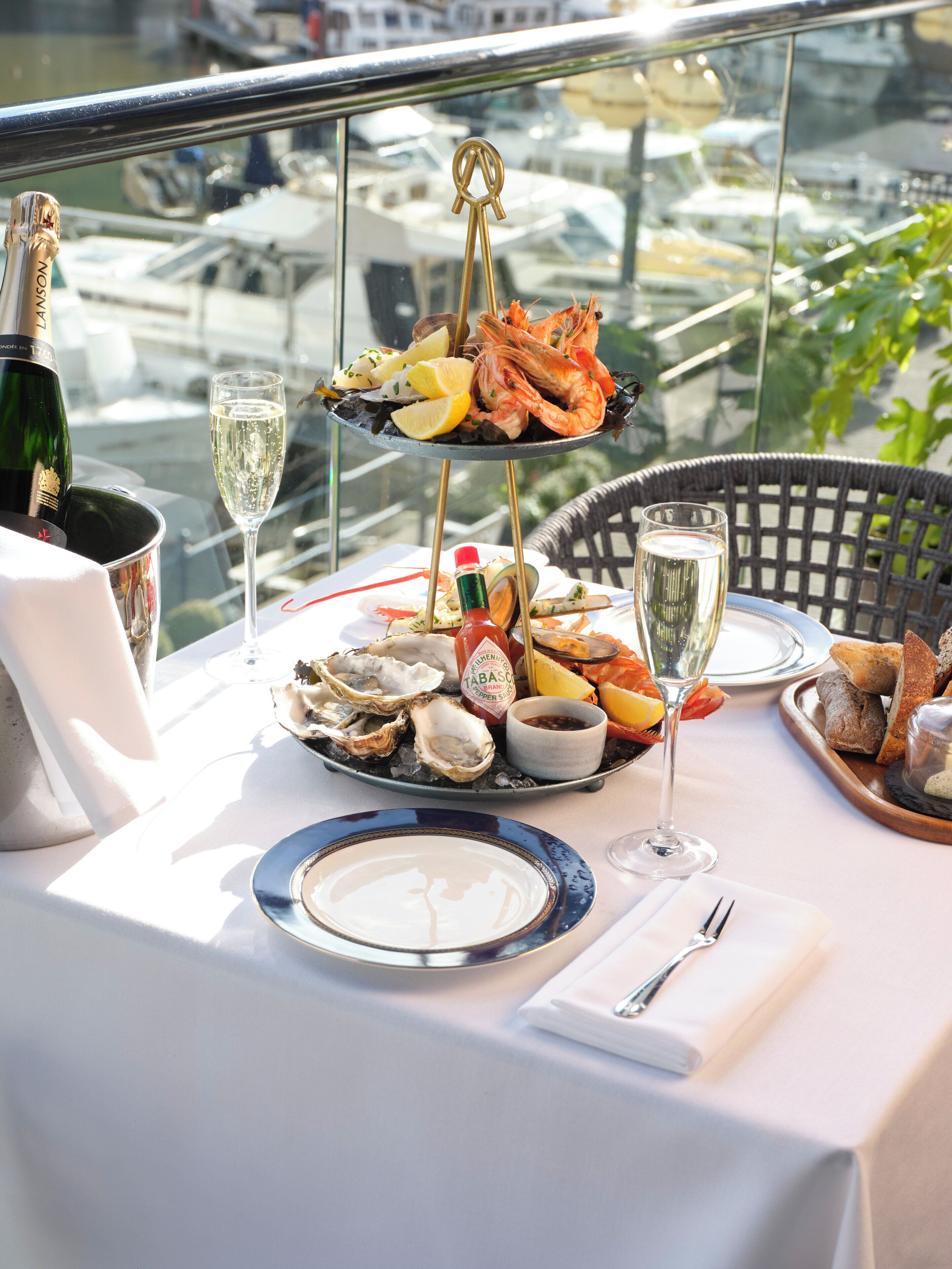 A table set for a meal with seafood, bread, and drinks, overlooking a marina.
