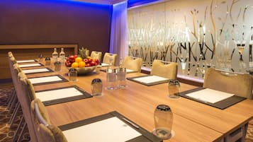 A conference room with a long table, chairs, a fruit bowl, water bottles, and a decorative wall.