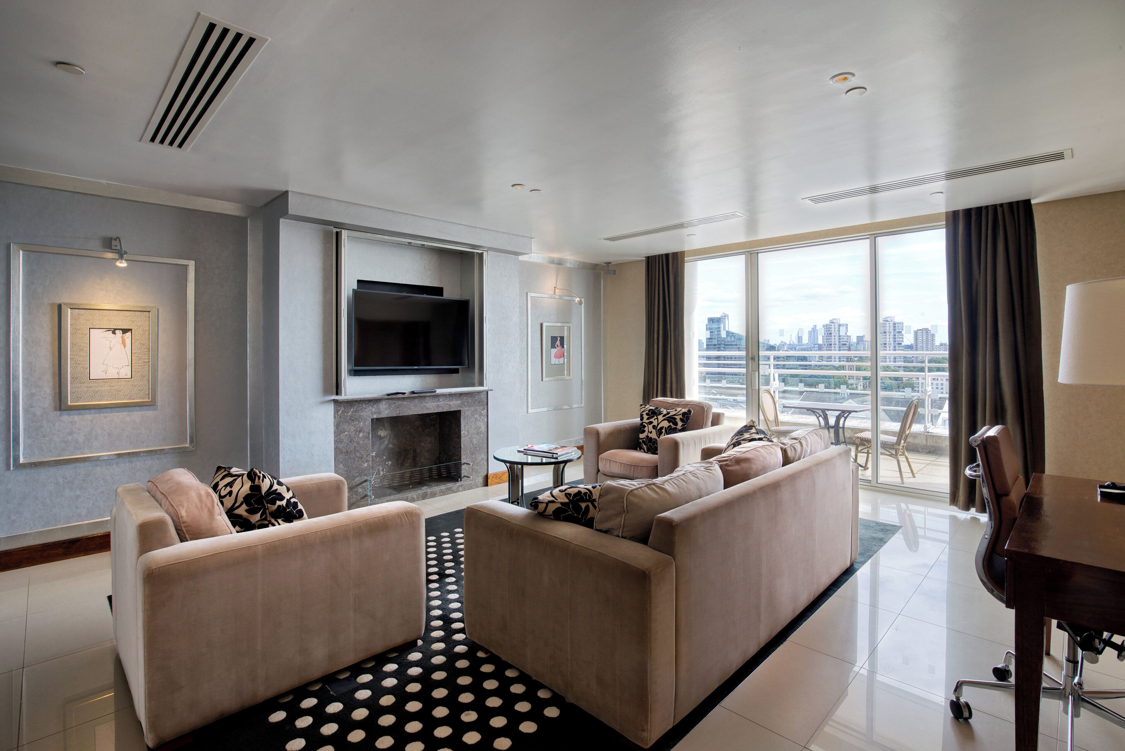 A modern living room with a sofa set, a fireplace, a flat-screen TV, and a city view through large windows.