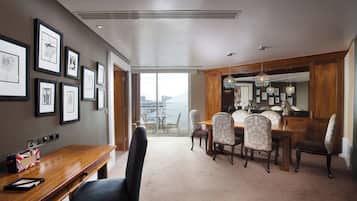 A hotel dining area with a wooden table and chairs, framed artwork on the walls, and a view through the glass door.