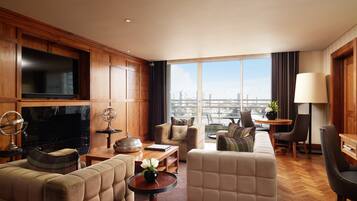 Un salón amplio con un televisor grande, asientos cómodos, una mesa de centro de madera y vistas de la ciudad a través de amplias ventanas.