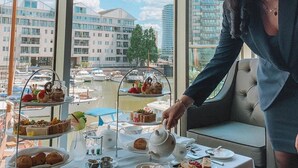Un coin repas avec une table dressée pour le service du thé, donnant sur une marina où l’on peut admirer des bateaux et des bâtiments.