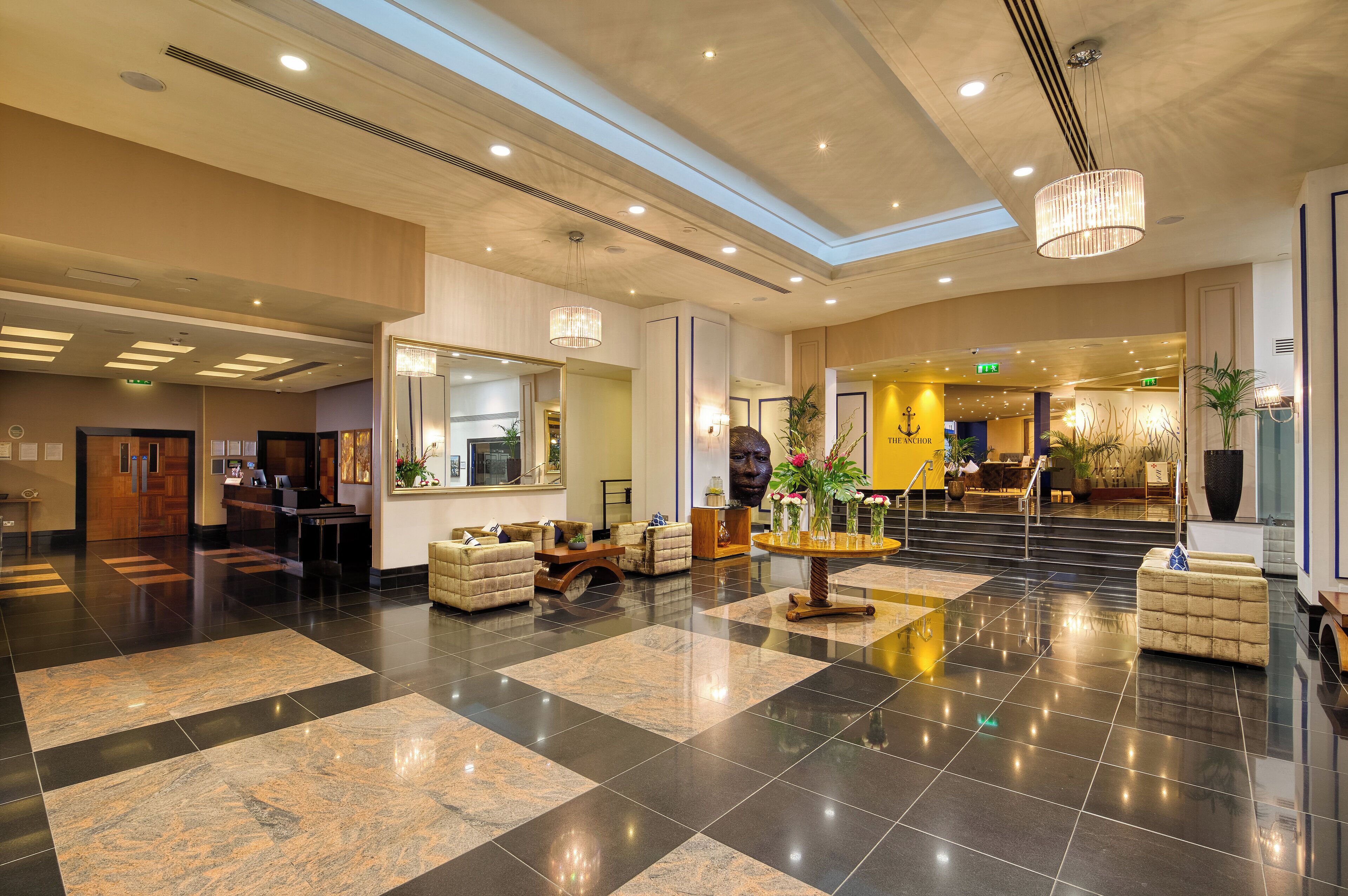 A spacious lobby with a checkered floor, a reception desk, seating areas, and a staircase leading to upper floors.