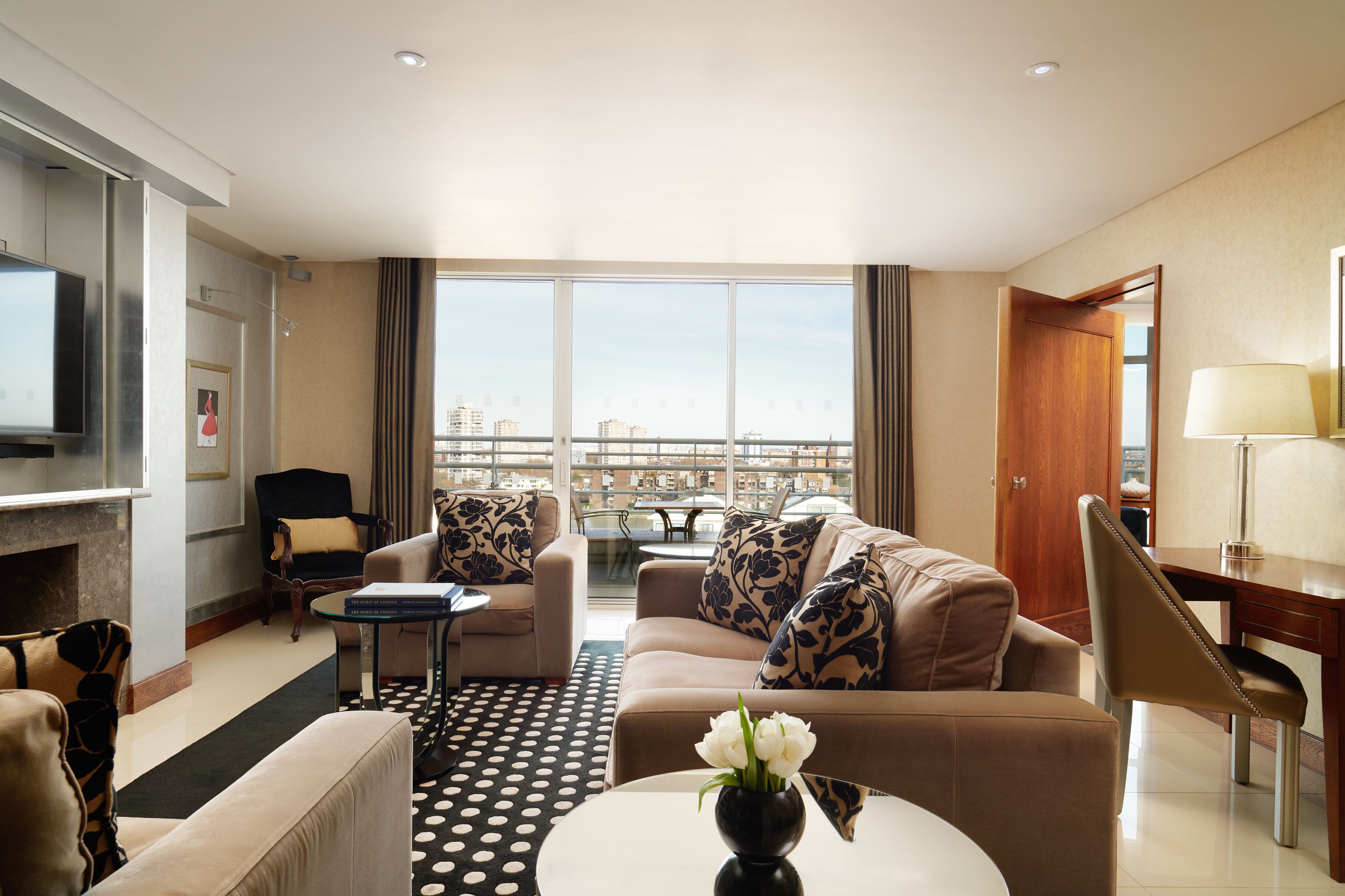 A hotel room with a sofa set, a TV, a dining table, and a view of the cityscape.