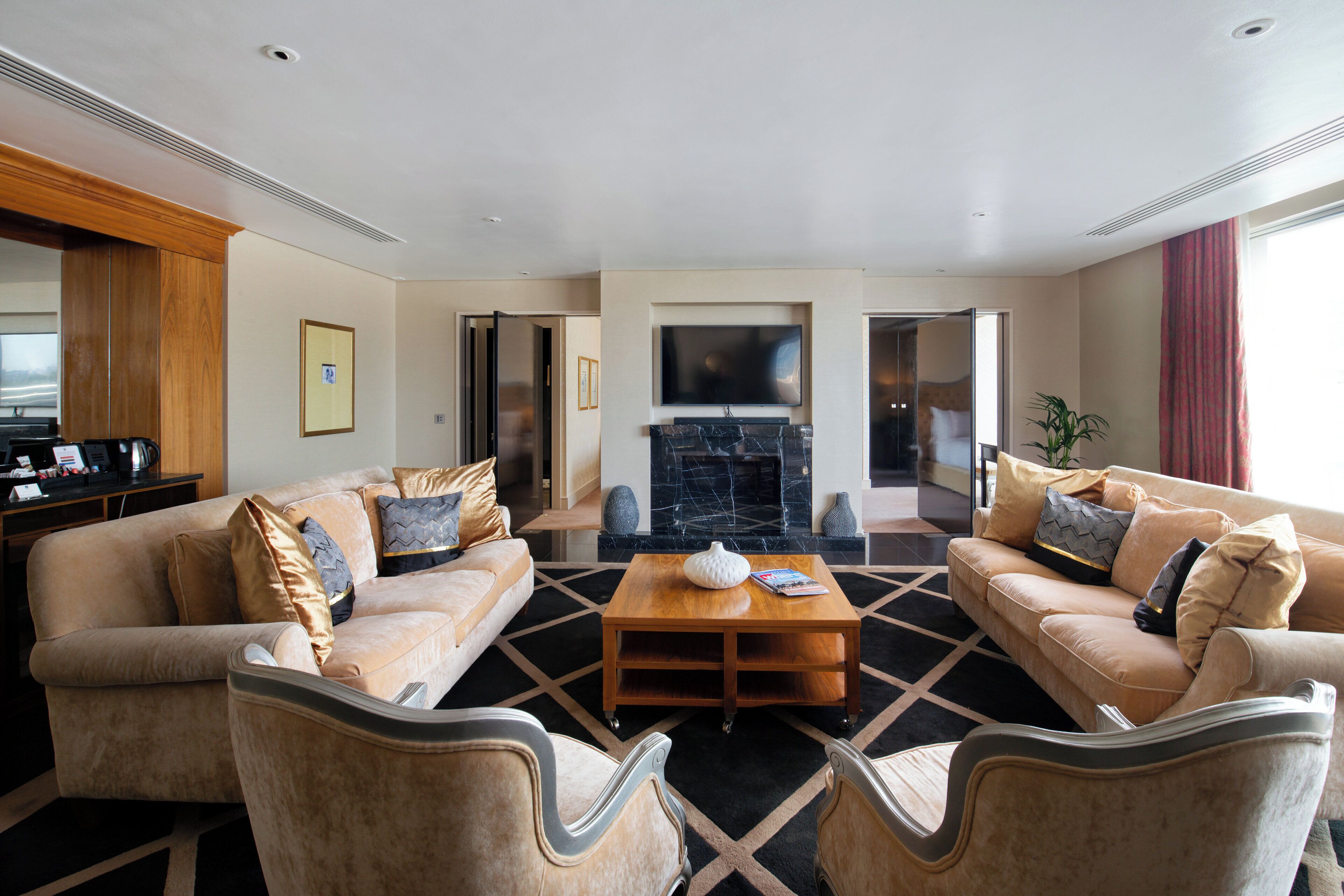 A spacious living room with beige sofas, a wooden coffee table, and a fireplace.