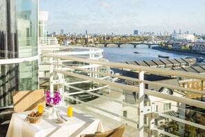 A balcony with a table set for breakfast, overlooking a river with bridges and buildings.