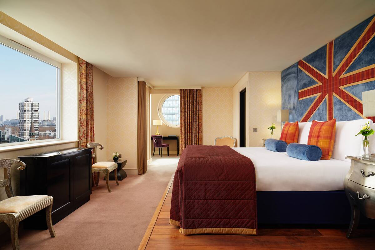 A hotel room with a large bed, a desk, a chair, and a view of the city.