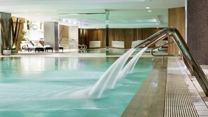 Une piscine intérieure moderne, dotée d’une eau claire, d’une paroi en verre et d’une échelle en métal.