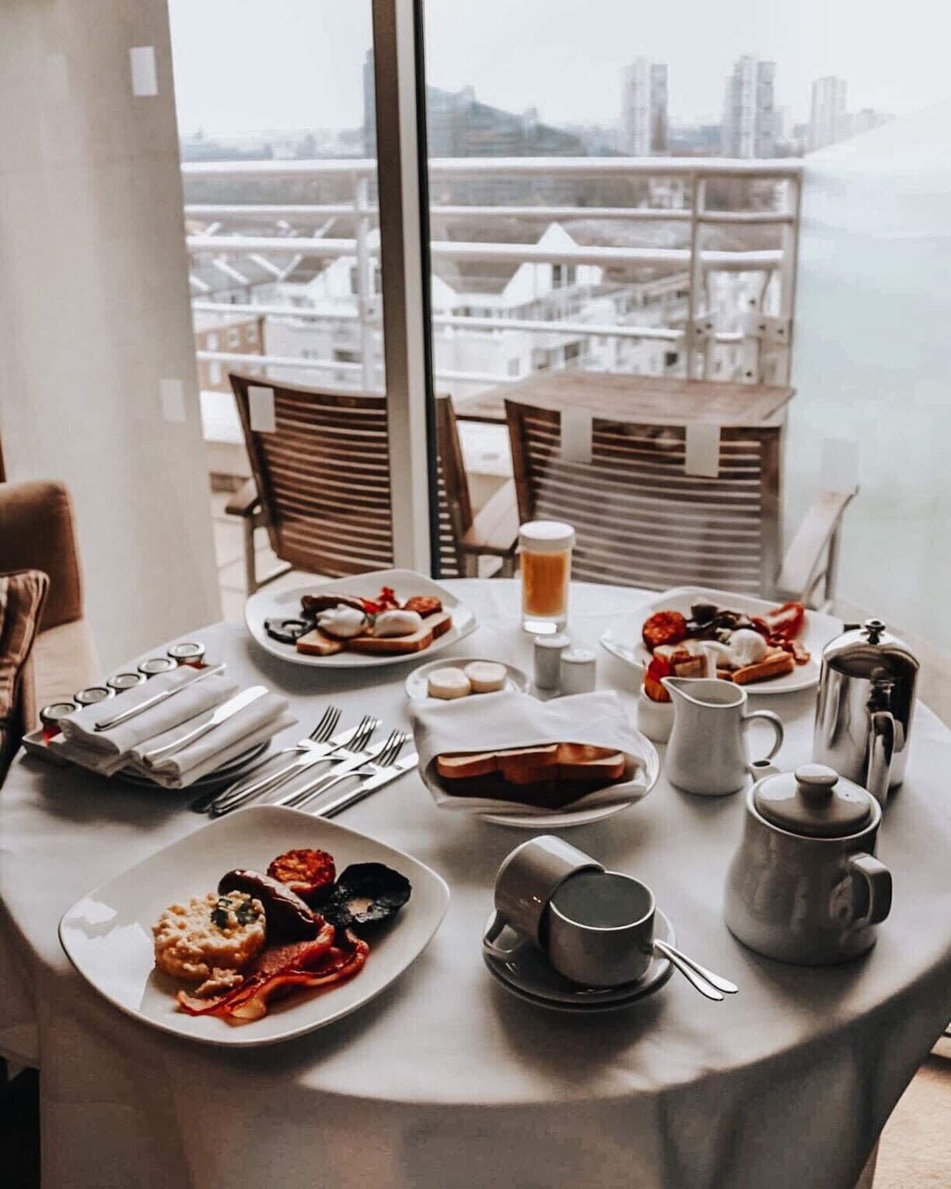 A dining table set with plates of food, cutlery, and a coffee pot, overlooking a cityscape.