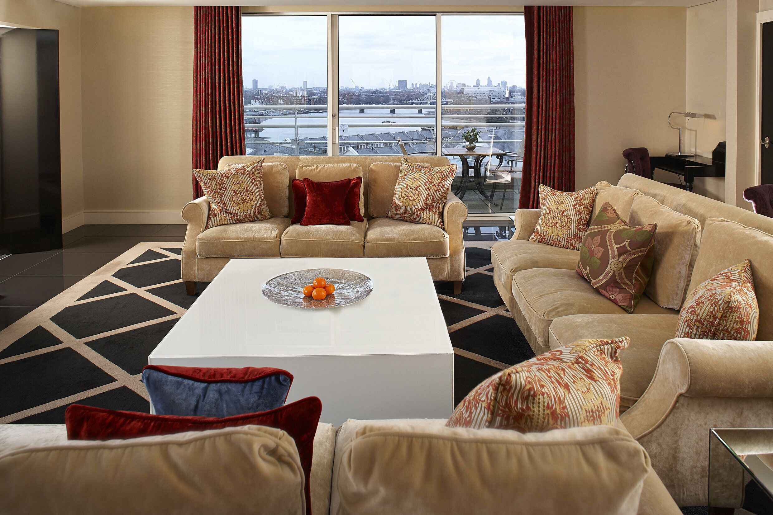 Amplia sala de estar con un gran ventanal que ofrece vistas a la ciudad, una mesa de centro blanca y dos sofás color beige con cojines estampados.