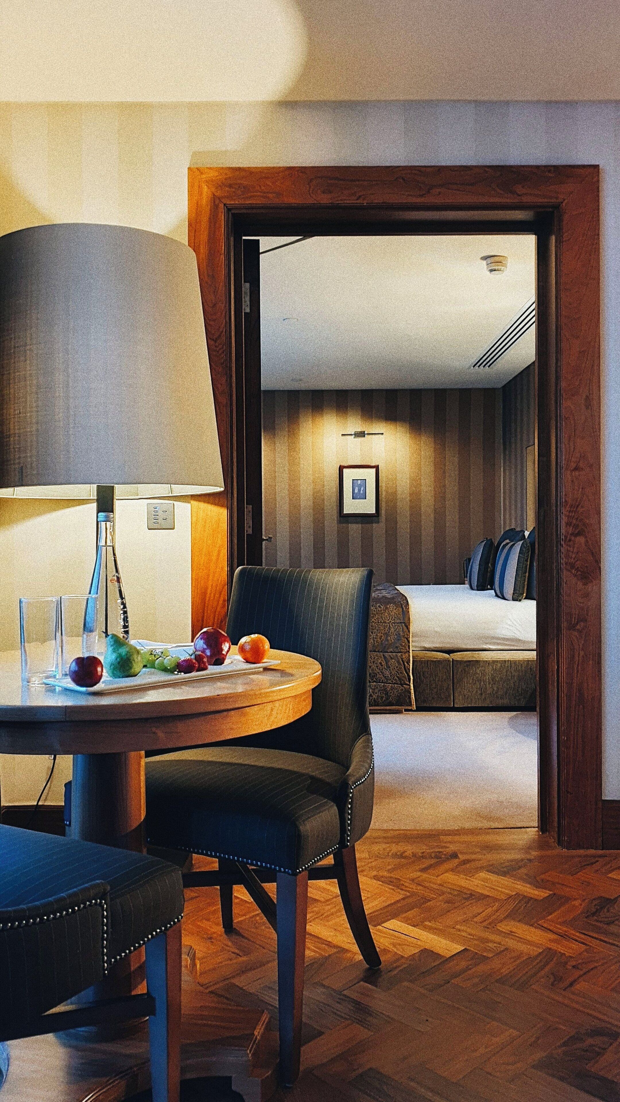Une chambre d’hôtel avec une table de salle à manger ronde, une chaise, une lampe et un lit avec des oreillers.