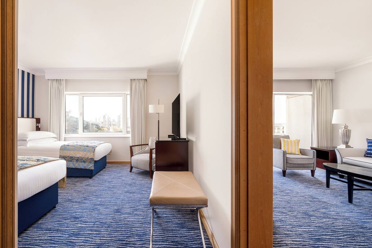 A hotel room with two beds, a bench, a desk, a chair, and a sofa.