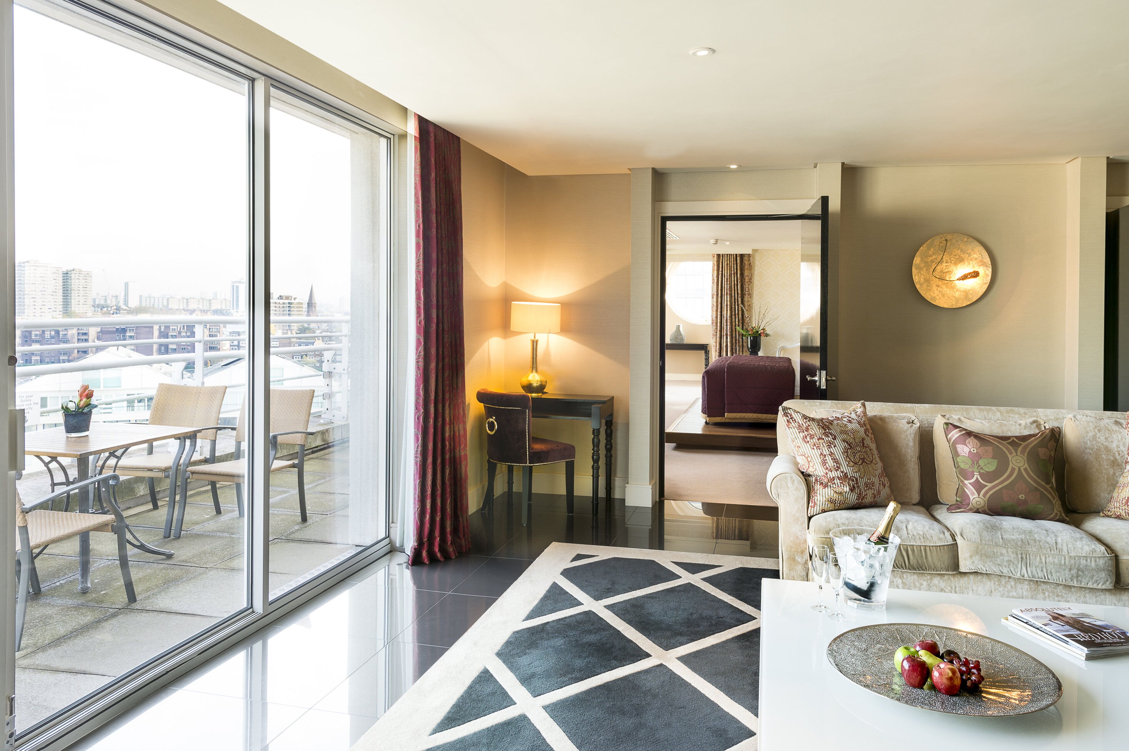 Una habitación de hotel moderna con balcón, zona de comedor, sofá y mesa de centro con fruta.