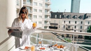 Un balcon aménagé pour le petit-déjeuner, avec des assiettes de nourriture, un verre de jus d’orange et un journal.