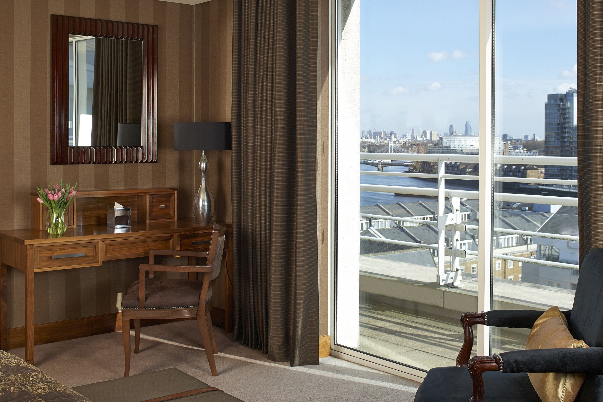 A hotel room with a desk, chair, and a large window offering a city view.