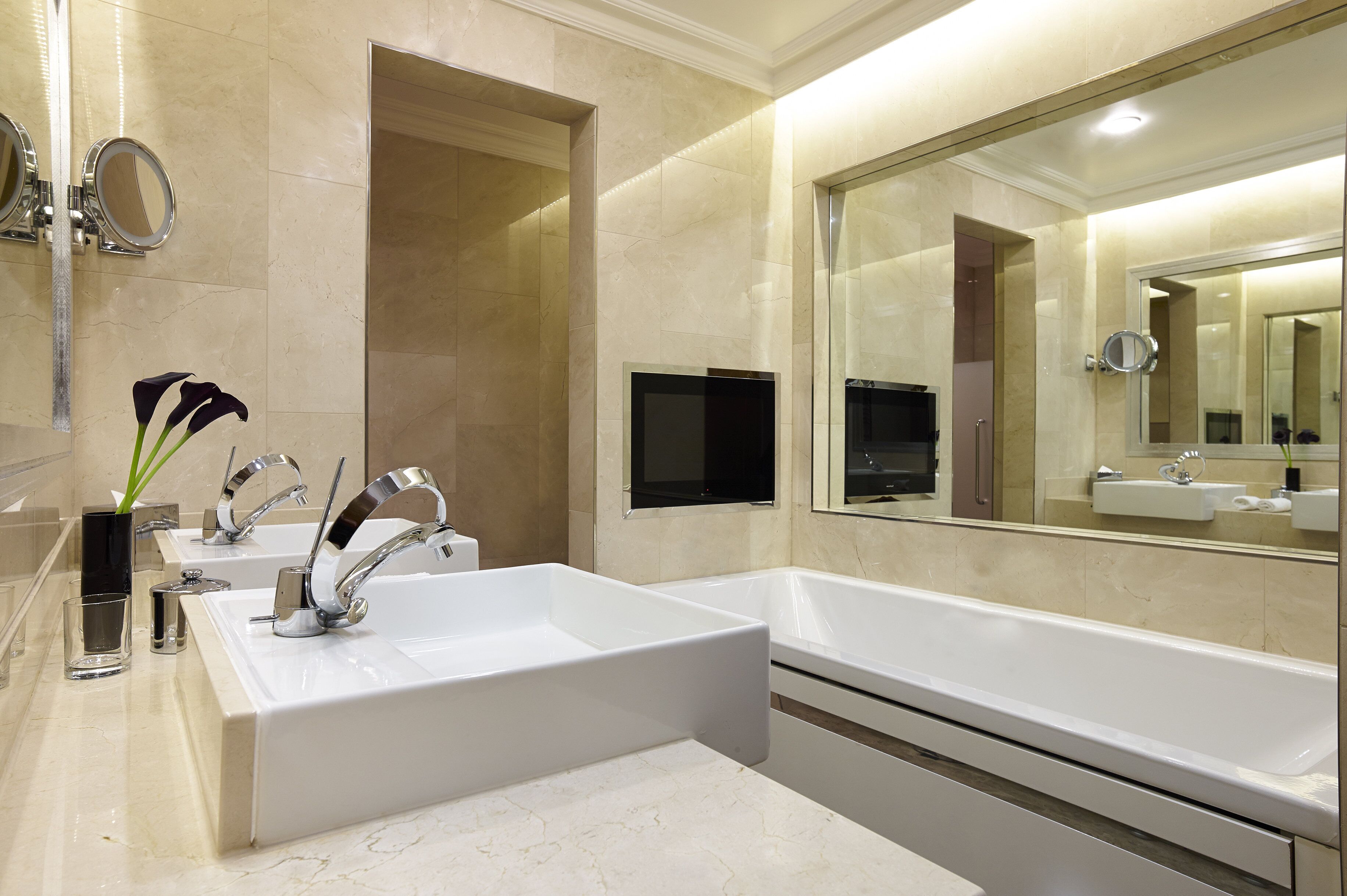 Une salle de bain moderne avec deux lavabos, un grand miroir et un téléviseur à écran plat.
