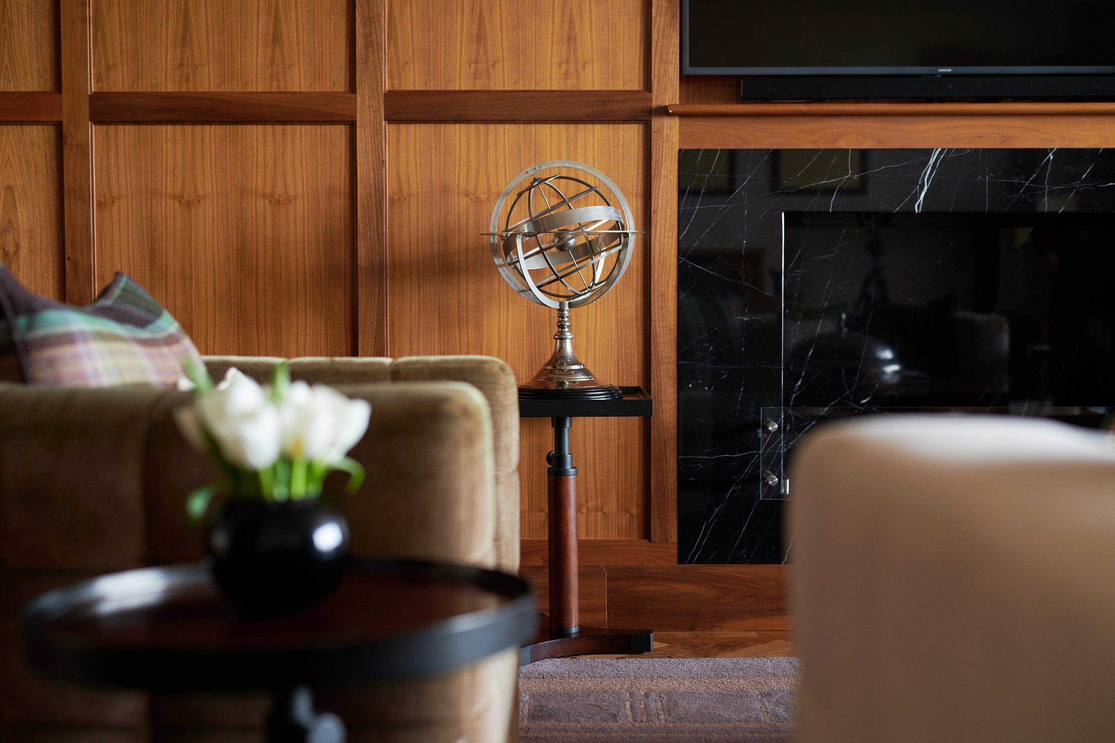 Una sala de estar acogedora con un revestimiento de madera, un globo terráqueo sobre un soporte, una chimenea y un sofá con un jarrón de flores.