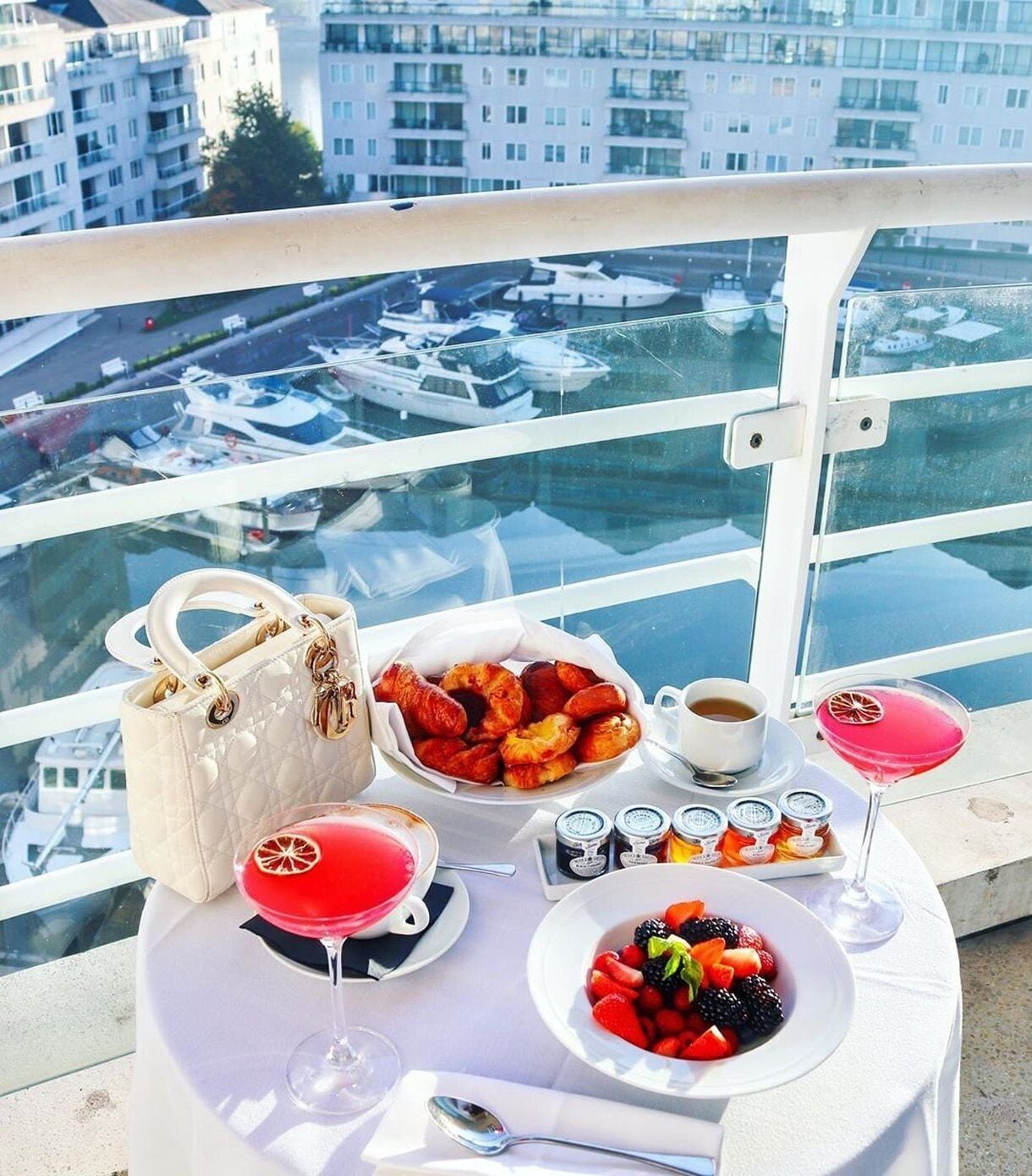 Un balcon avec une table préparée pour le petit-déjeuner, comprenant des viennoiseries, des fruits, du café et un cocktail.
