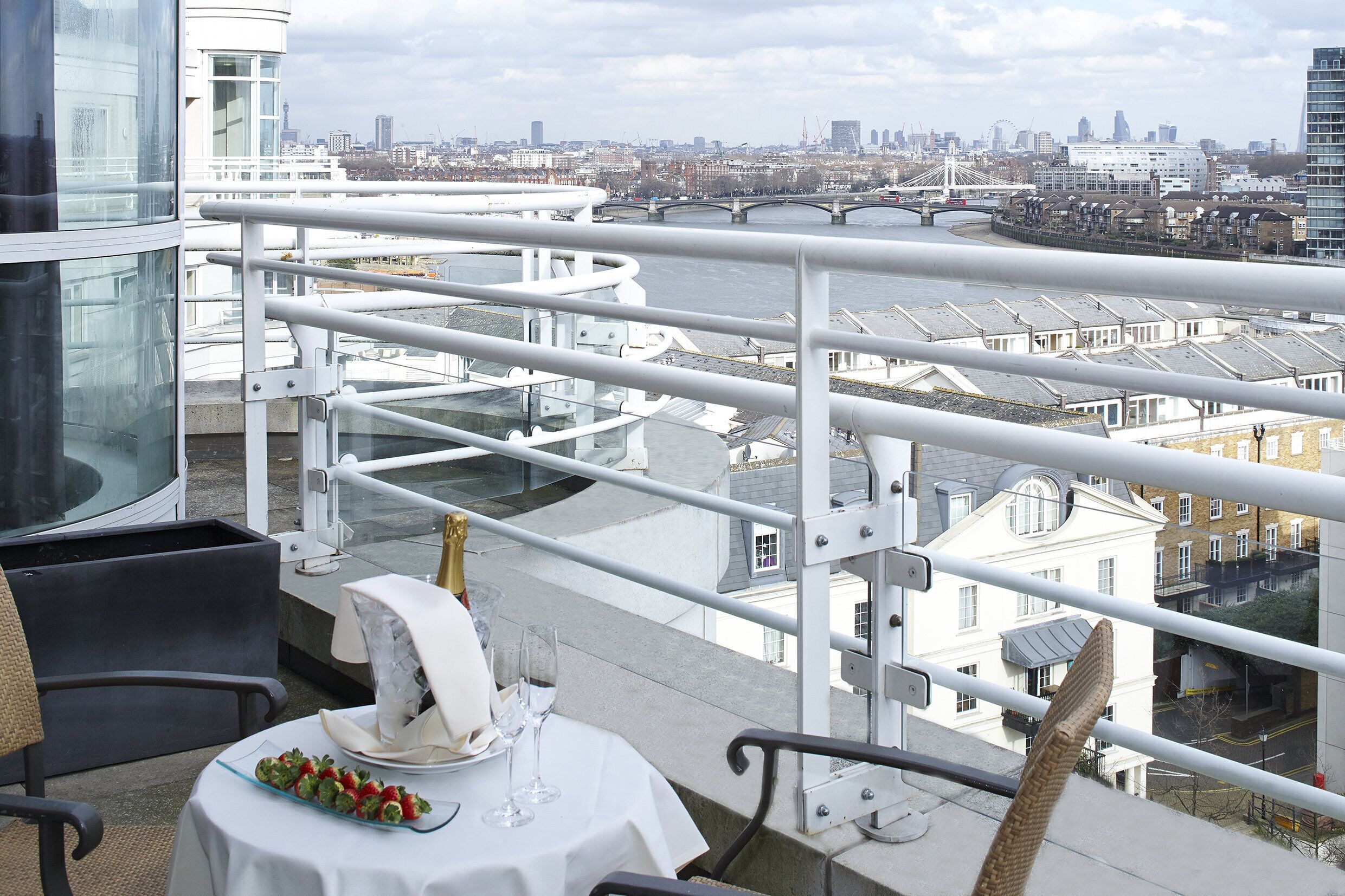 Un balcón con una mesa dispuesta para comer, con vistas a un paisaje urbano que incluye edificios y un río.
