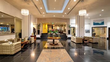 A spacious lobby with a central round table, sofas, and a staircase leading to an upper level.