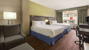 Ein Hotelzimmer mit zwei Betten, einem Schreibtisch, einem Sessel und einem Fernseher.