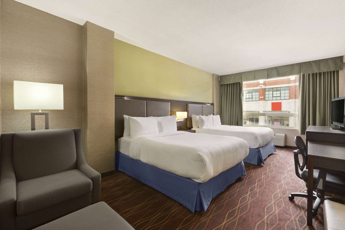 A hotel room with two beds, a desk, a chair, and a TV.
