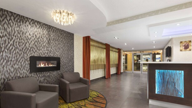 Eine Lobby mit Kamin, zwei Sesseln, einer Wand mit Muster und einem Empfangstresen mit Digitalanzeige.