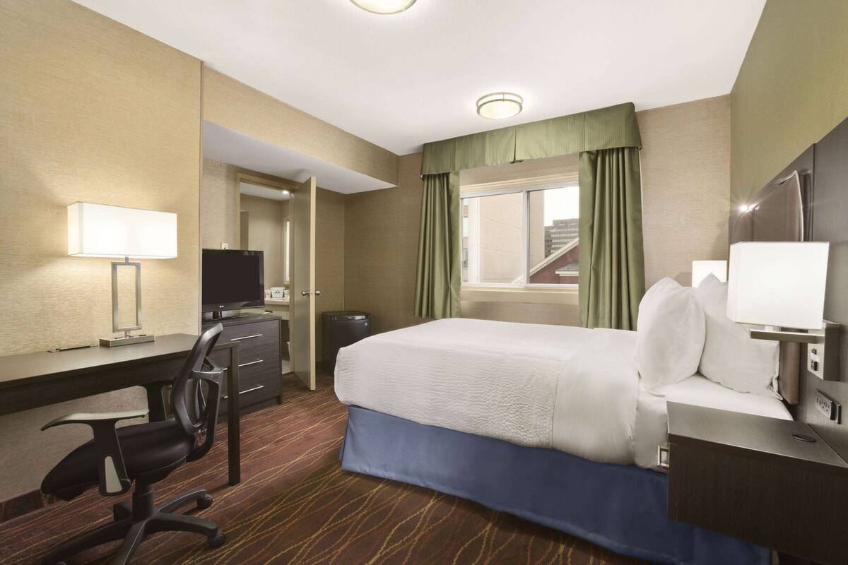 A hotel room with a bed, desk, chair, and a television.