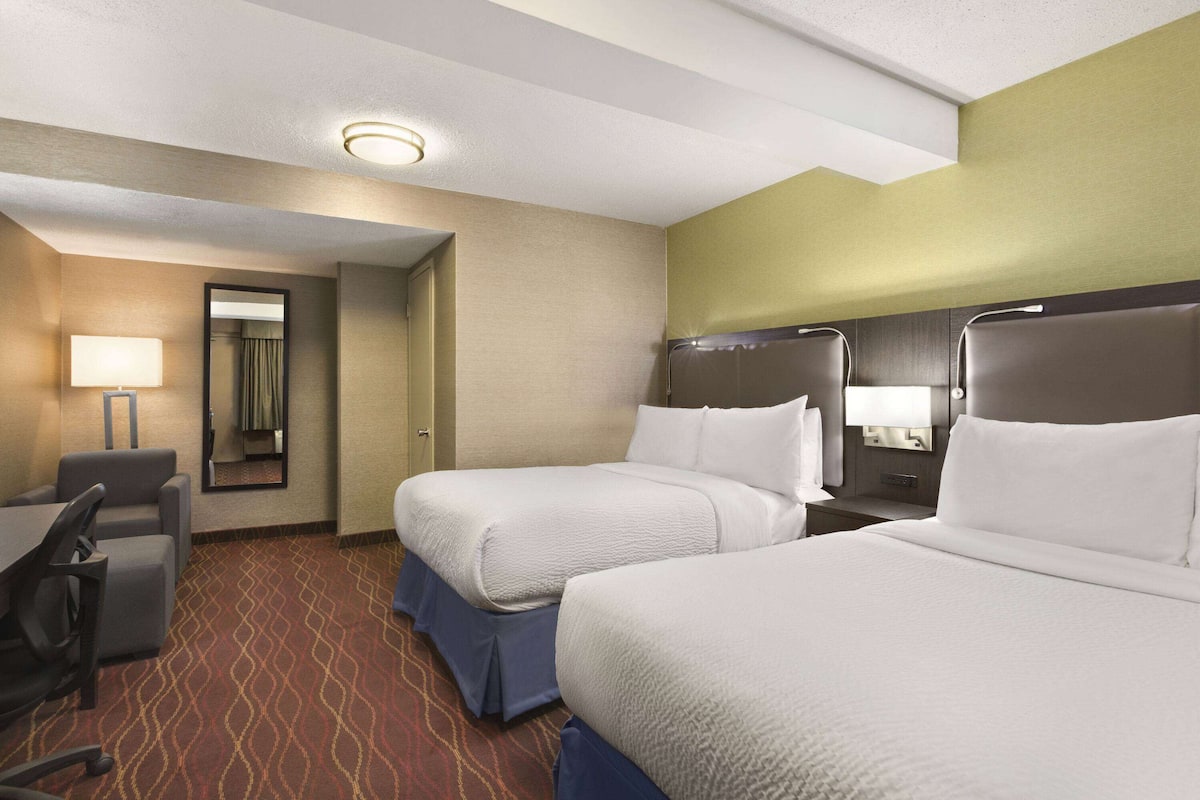 A hotel room with two beds, a desk, and a chair.