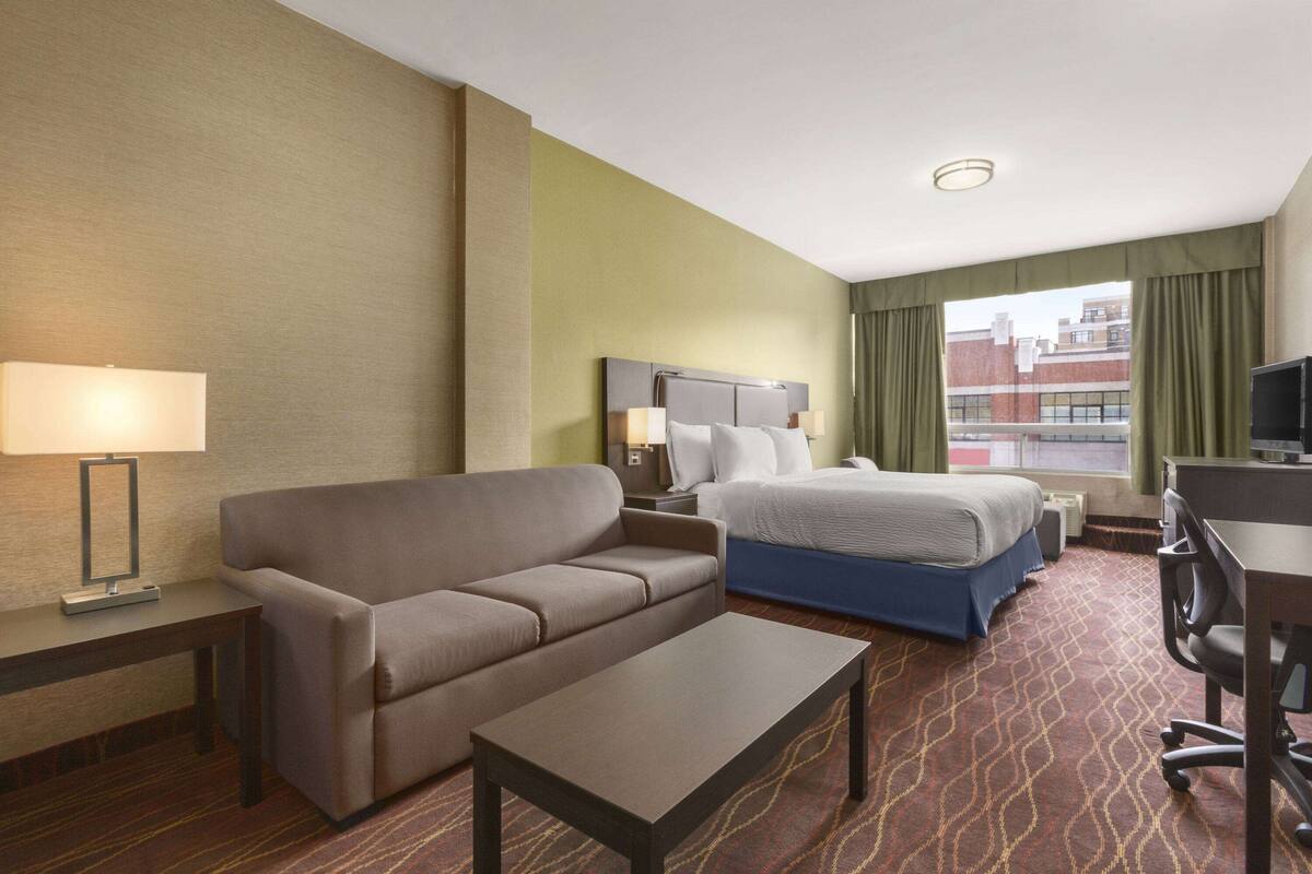 A hotel room with a sofa, a bed, a desk, and a TV.