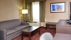 Ein Hotelzimmer mit einer Couch, einem kleinen Tisch, einer Bank, einem Schreibtisch, einer Lampe und einem gerahmten Bild an der Wand.