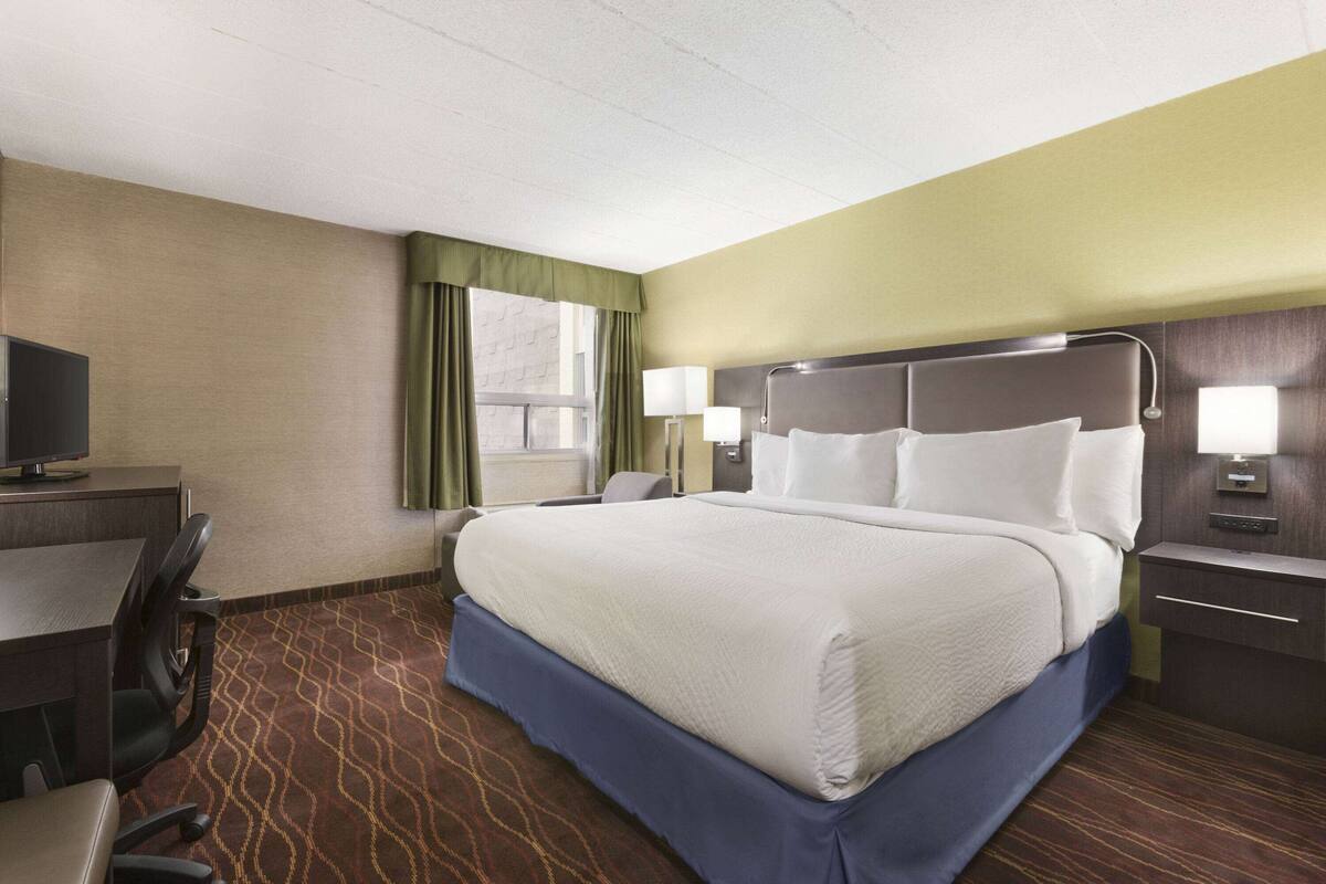 A hotel room with a large bed, a desk with a chair, a television, and two bedside lamps.