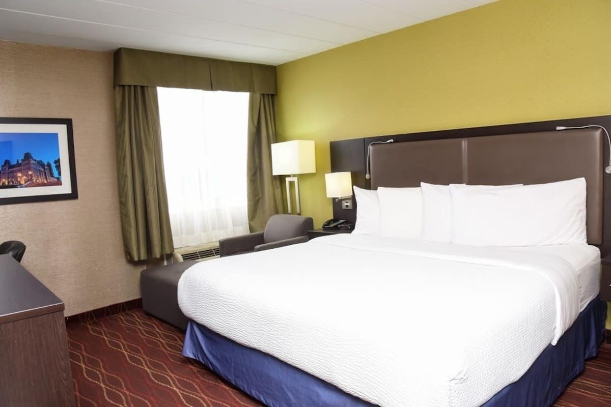 A hotel room with a large bed, a desk, a chair, a lamp, and a picture on the wall.