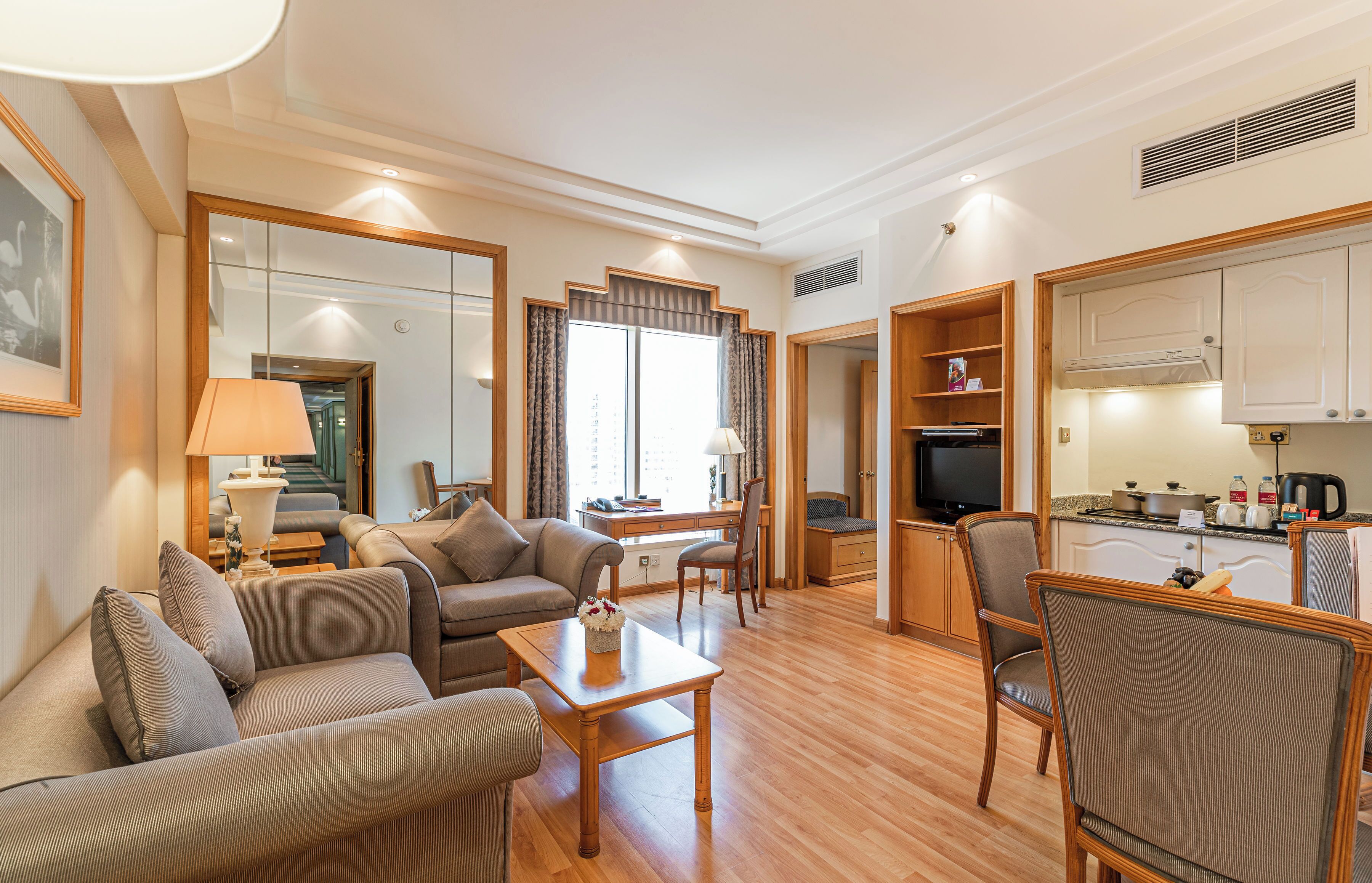 A spacious living area with a sofa, armchairs, a coffee table, and a television. There is a kitchen area with cabinets and a stove.