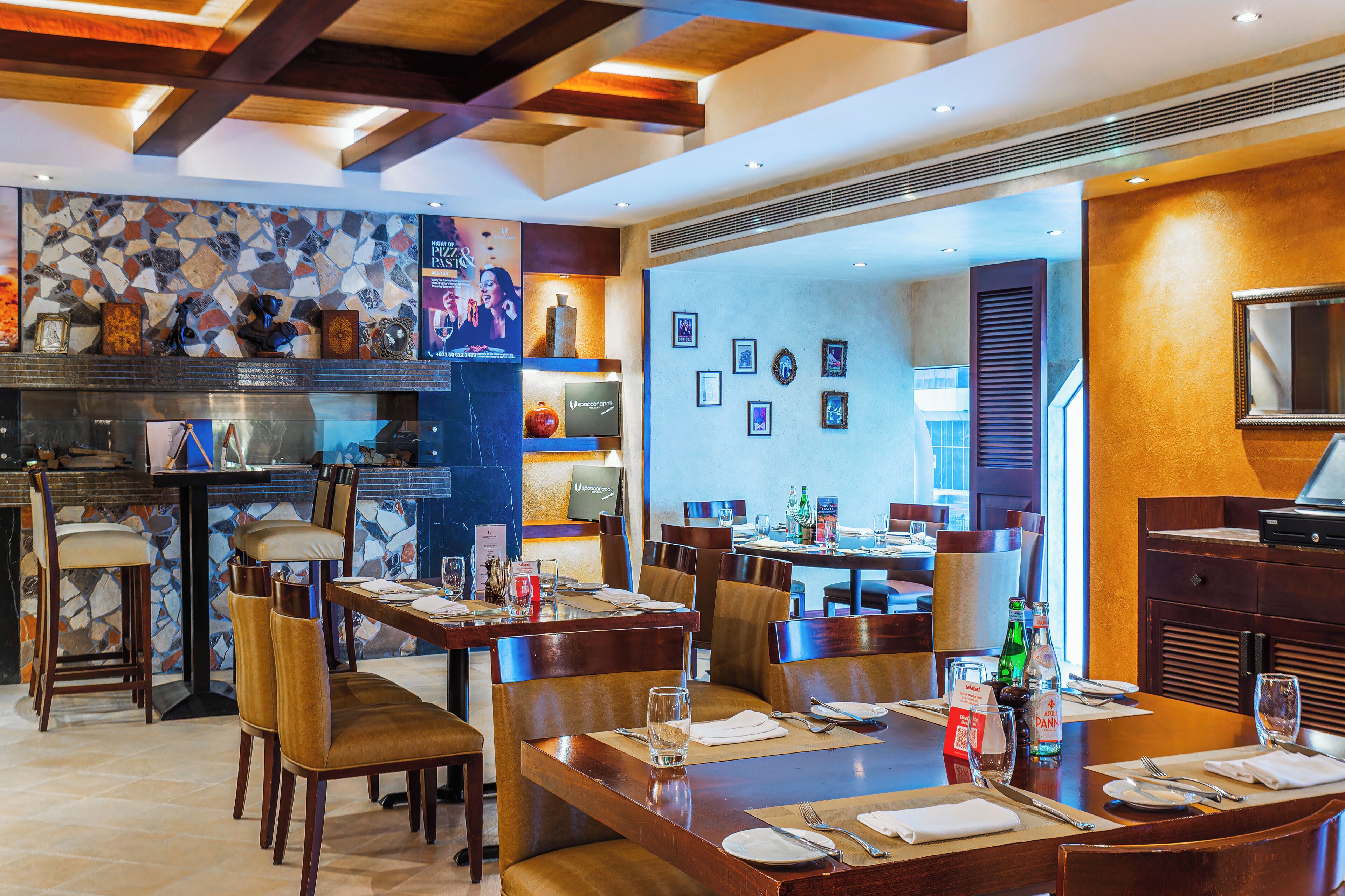 A restaurant with wooden tables and chairs, a tiled backsplash, and framed pictures on the wall.