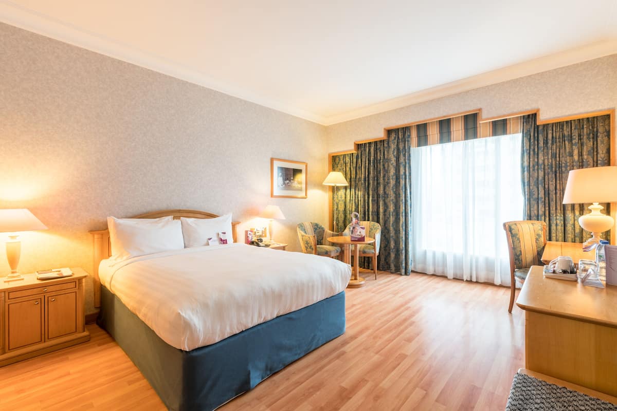 Een hotelkamer met een groot bed, nachtkastjes met lampen, een bureau met stoel, en een raam met gordijnen.