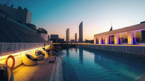 Una piscina en la azotea con sillones de descanso y vistas al perfil urbano al anochecer.