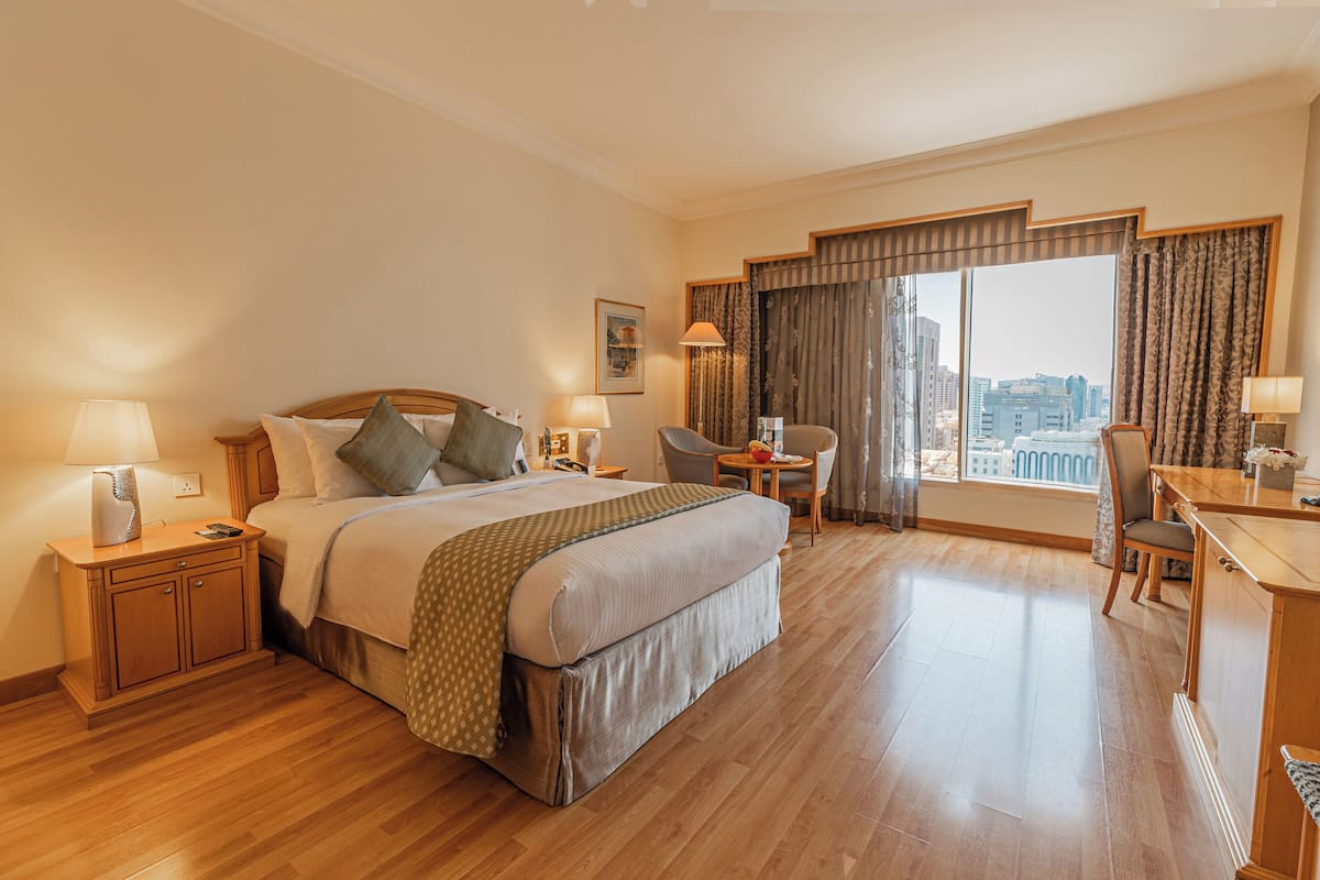 Een hotelkamer met een groot bed, een bureau, een stoel en uitzicht op de stad.