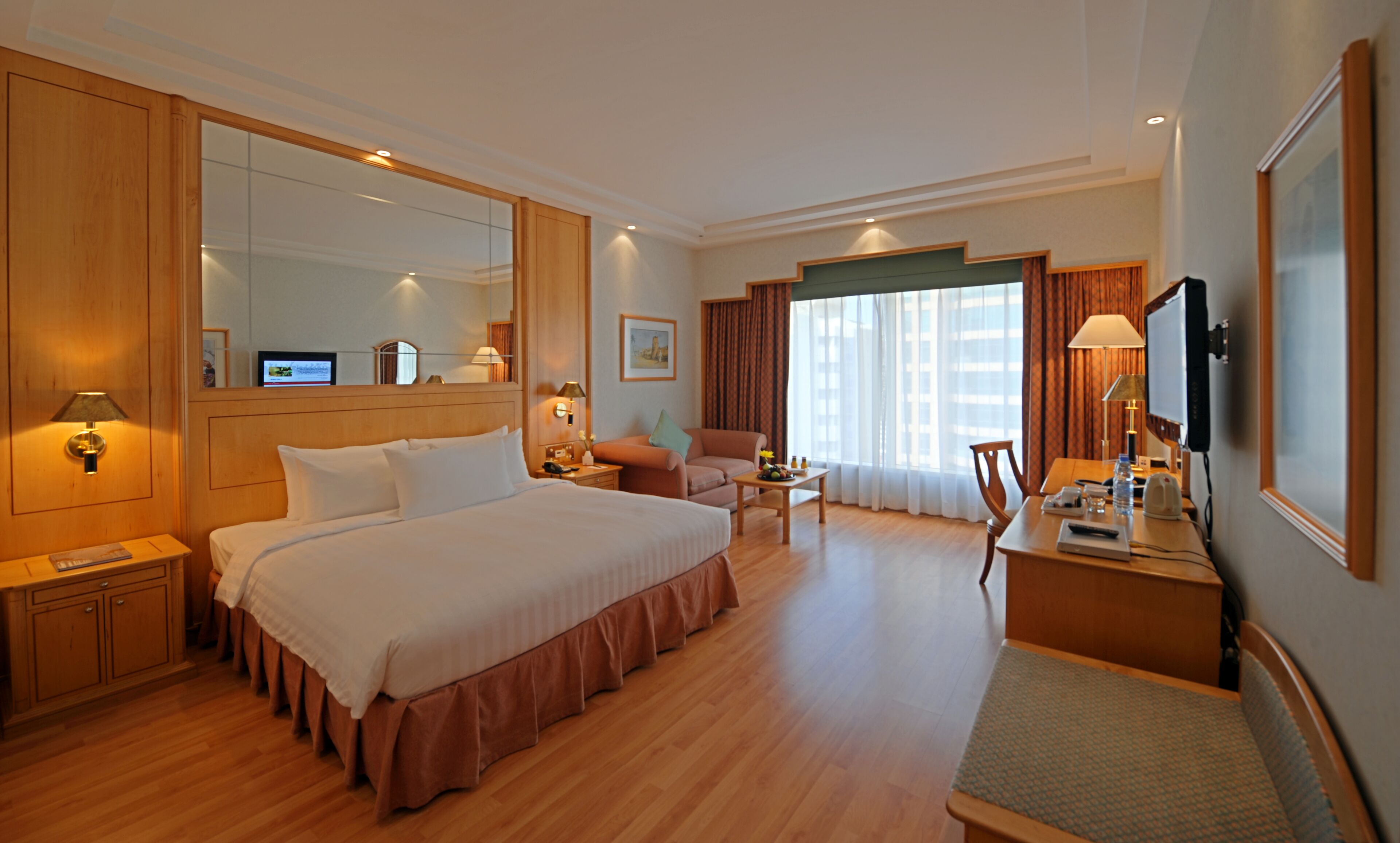 Quarto de hotel com uma cama grande, uma escrivaninha, uma cadeira, uma televisão e uma janela com cortinas.