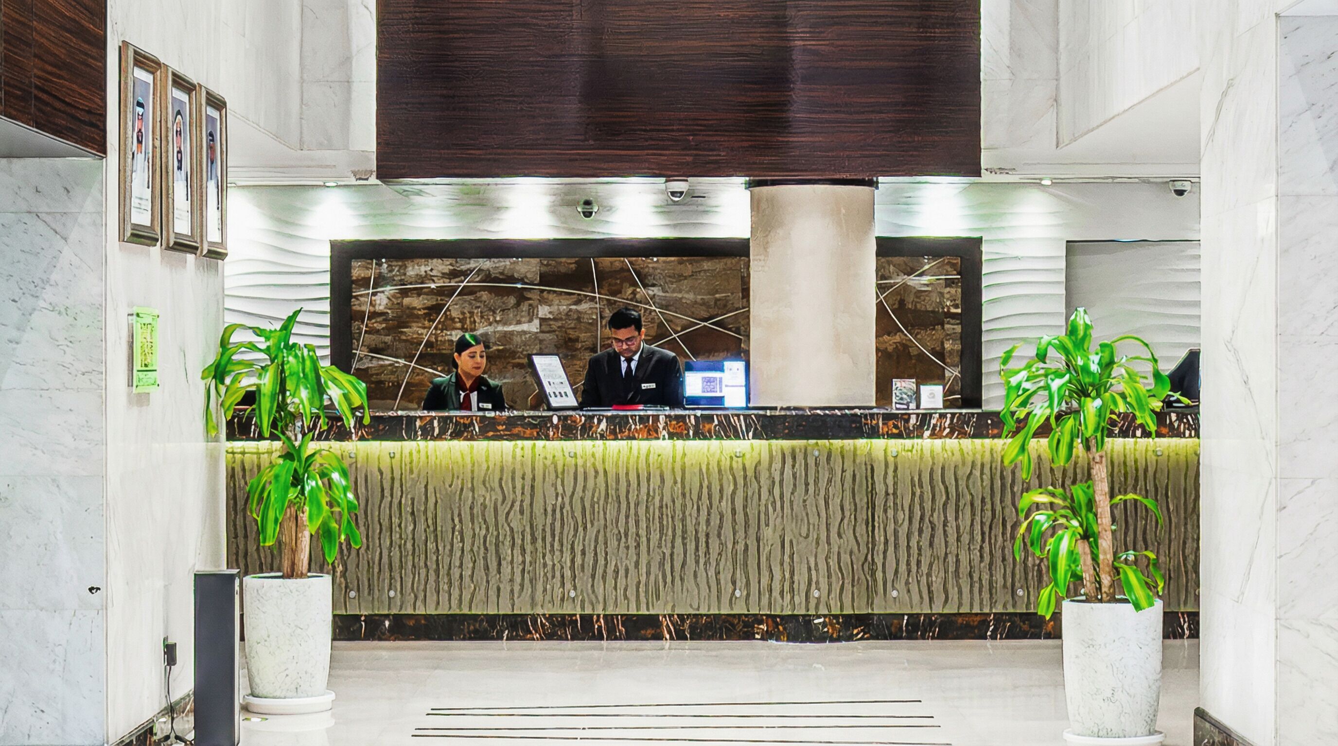 A reception desk with two receptionists, a modern design with a textured wall, and potted plants.