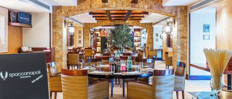 Un restaurant doté d’une arche en pierre, de poutres en bois au plafond et d’une plante au centre. Les tables sont disposées avec des chaises, et un ordinateur portable est posé sur un support.