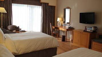 Ein Hotelzimmer mit zwei Betten, einem Schreibtisch mit Stuhl, einem Fernseher und einem Schrank.