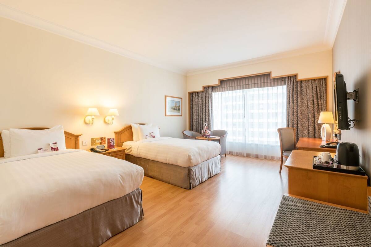 A hotel room with two beds, a desk, a chair, a TV, and a window with curtains.